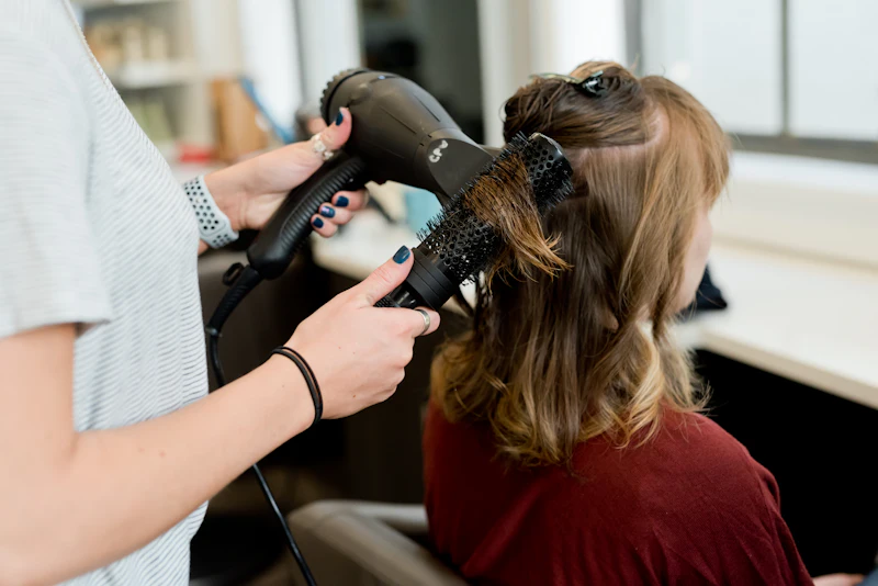 Cabeleireira secando o cabelo de uma cliente com escova redonda